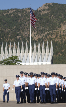 Cadets marching with Chapel and flag in the background.